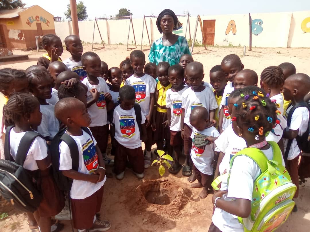 Children planting a seedling in the schoolyard at Medina Kanuma